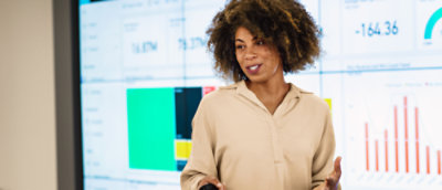 A woman with curly hair interacts with a computer screen, extending her hand towards it.