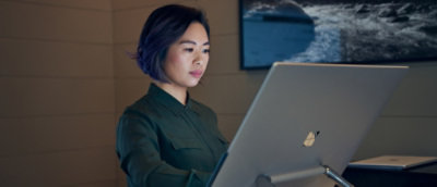 A woman working attentively on a desktop computer in a dimly lit modern office environment