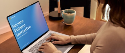 Person working on a laptop displaying a Microsoft Secure Future Initiative report at a desk with a coffee mug.