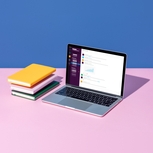 Bücherstapel neben einem aufgeklappten Laptop, auf dem die Slack-Anwendung zu sehen ist