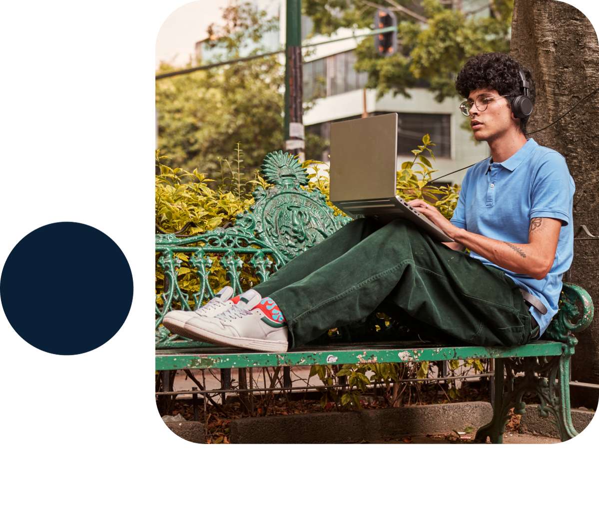 An individual wearing headphones outside and sitting on a bench with their laptop.