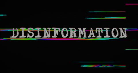 The image shows the word “DISINFORMATION” in white capital letters on a black background. The text has a digital glitch effect with streaks of green and pink distorting the letters, suggesting a theme of corrupted data or misleading information.
