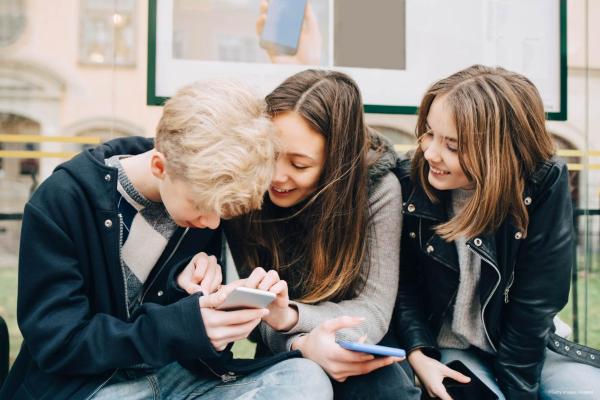 Three young children sitting looking at a smartphone
