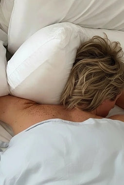 Person lying on a bed with white pillows and bedding