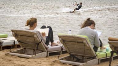 Two European holidaymakers lie on sunloungers in Western Sahara, while another kite surfs in the sea