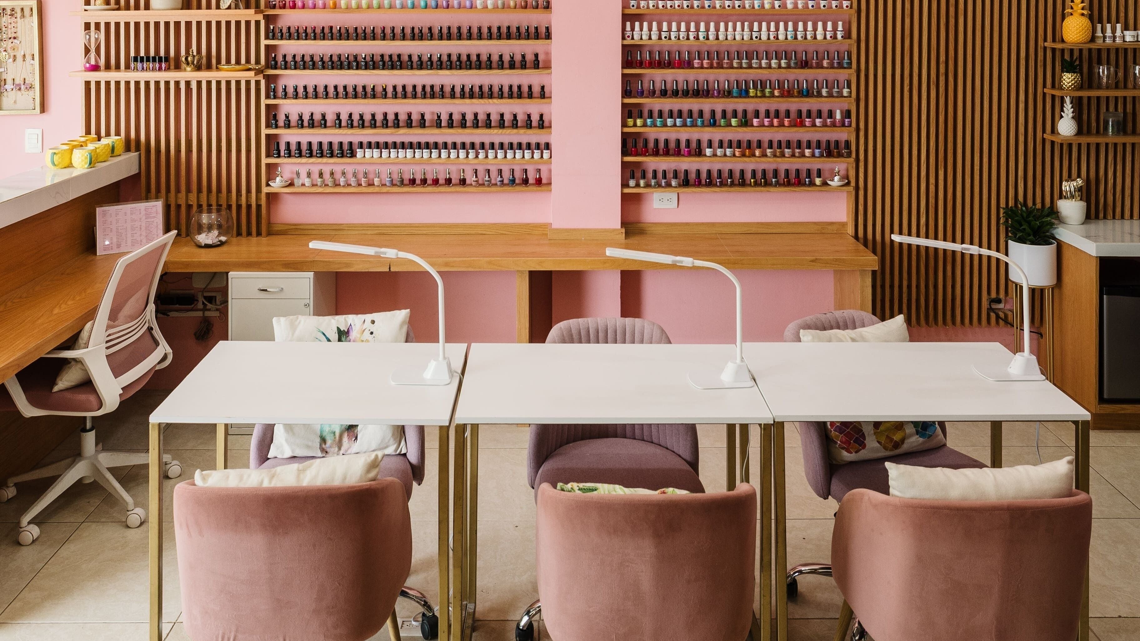 Interior moderno de Piña Nails Room en Mérida, Yucatán, MX, con sillas rosadas y extensa colección de esmaltes.