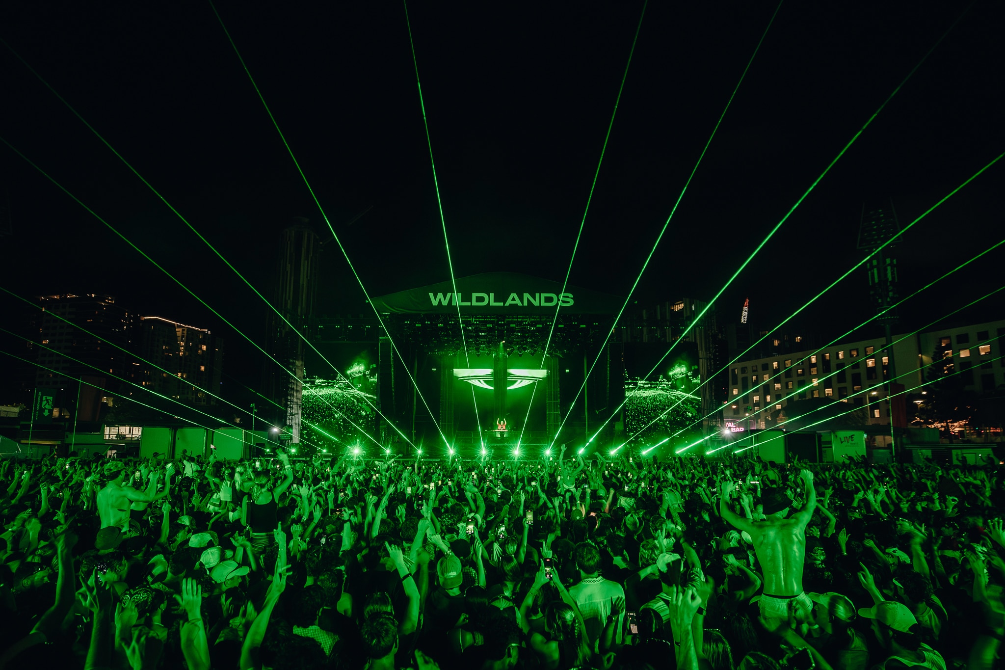A festival crowd at night in front of a stage with green lasers, the crowd is lit up green
