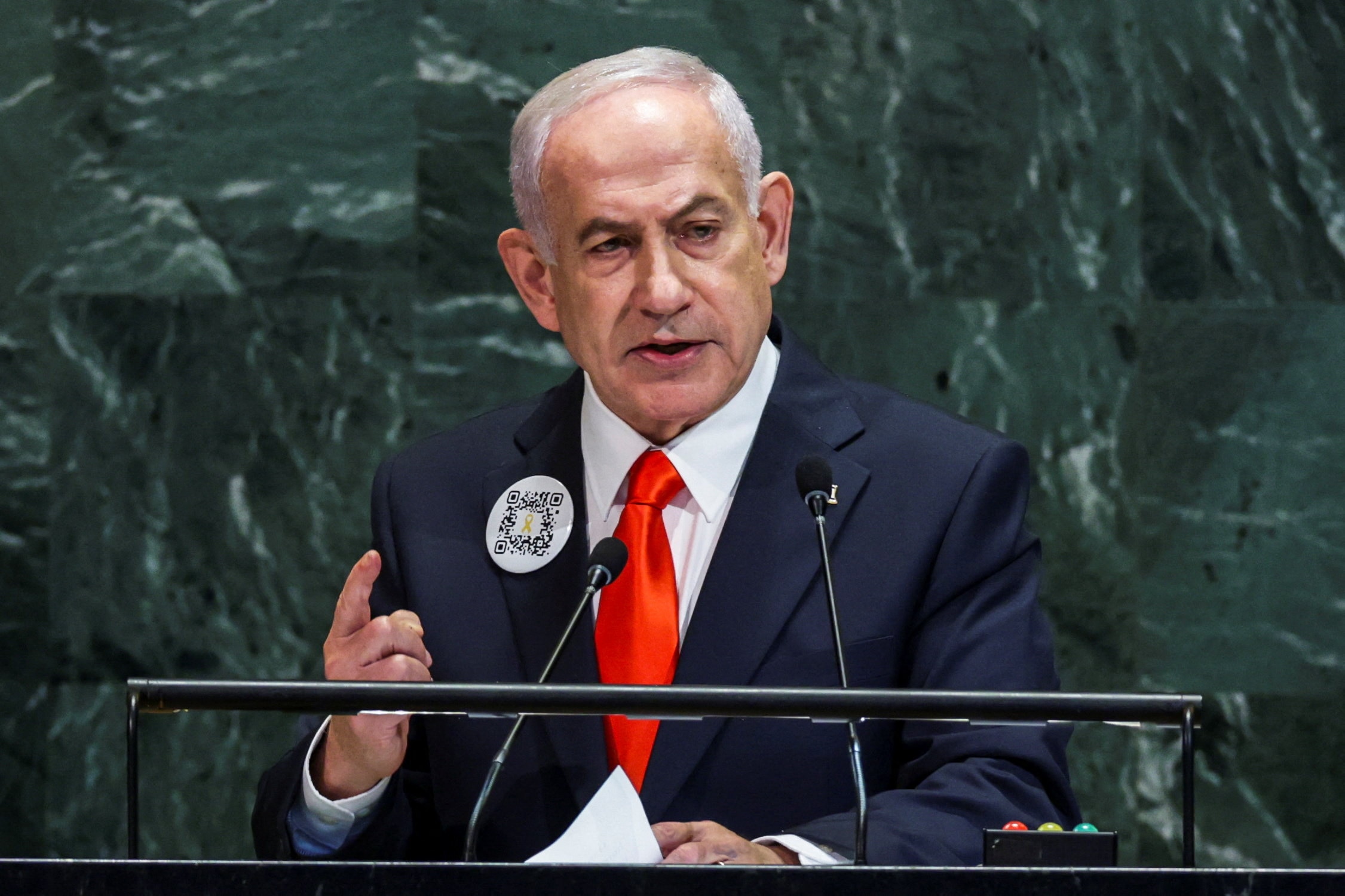 Benjamin Netanyahu addresses the UN from a podium, with a QR code pinned to his blazer.
