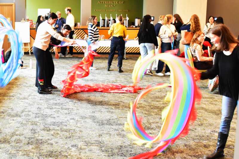 Dancers perform with vibrant, colorful ribbons and fabric in a spacious hall during a lively indoor cultural event.