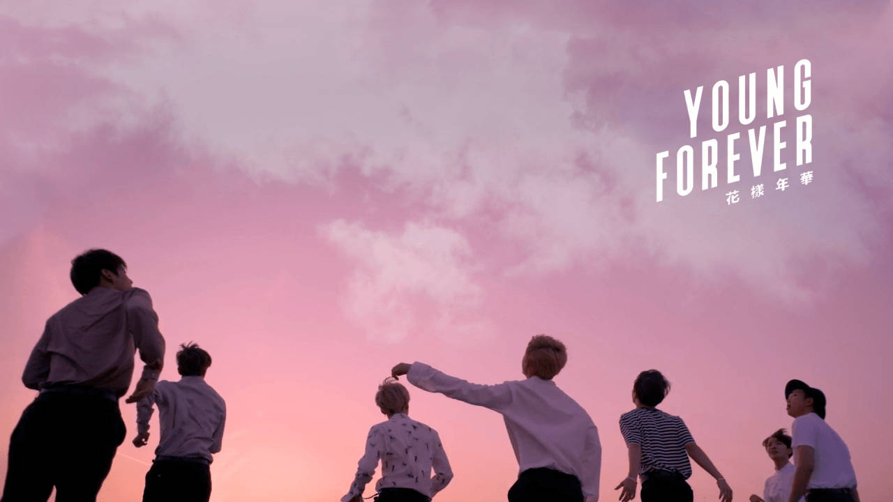 Seven young men silhouetted against a pink sunset sky with clouds.