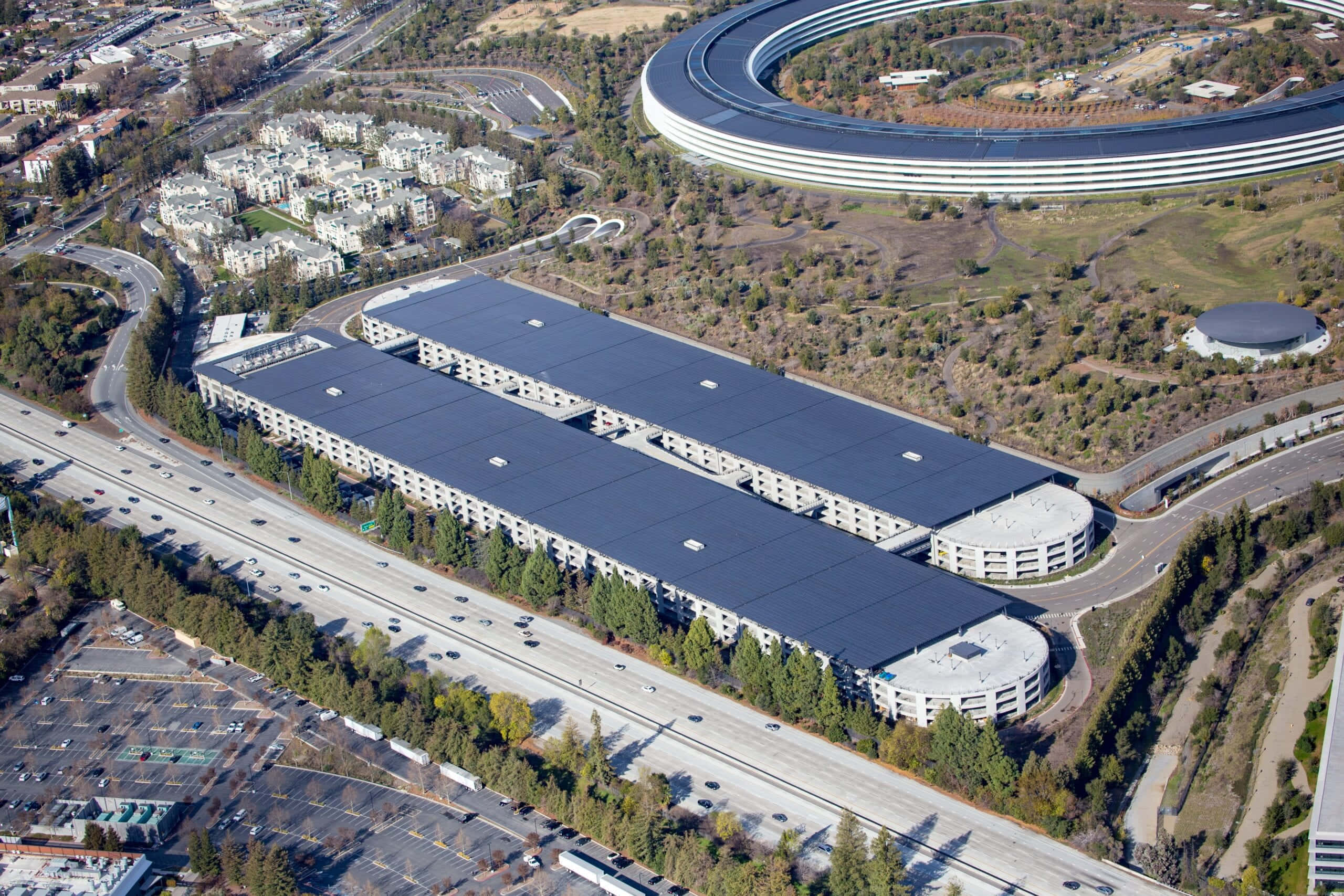 Questa immagine presenta una splendida vista aerea dell'Apple Park, la sede centrale di Apple Inc., situata a Cupertino, California. L'architettura circolare futuristica della struttura è evidenziata, mostrando l'estetica del design innovativo per cui Apple è rinomata. La rigogliosa vegetazione che circonda la struttura sottolinea il suo impegno verso un'infrastruttura ecologica. — Apple Store Sfondi