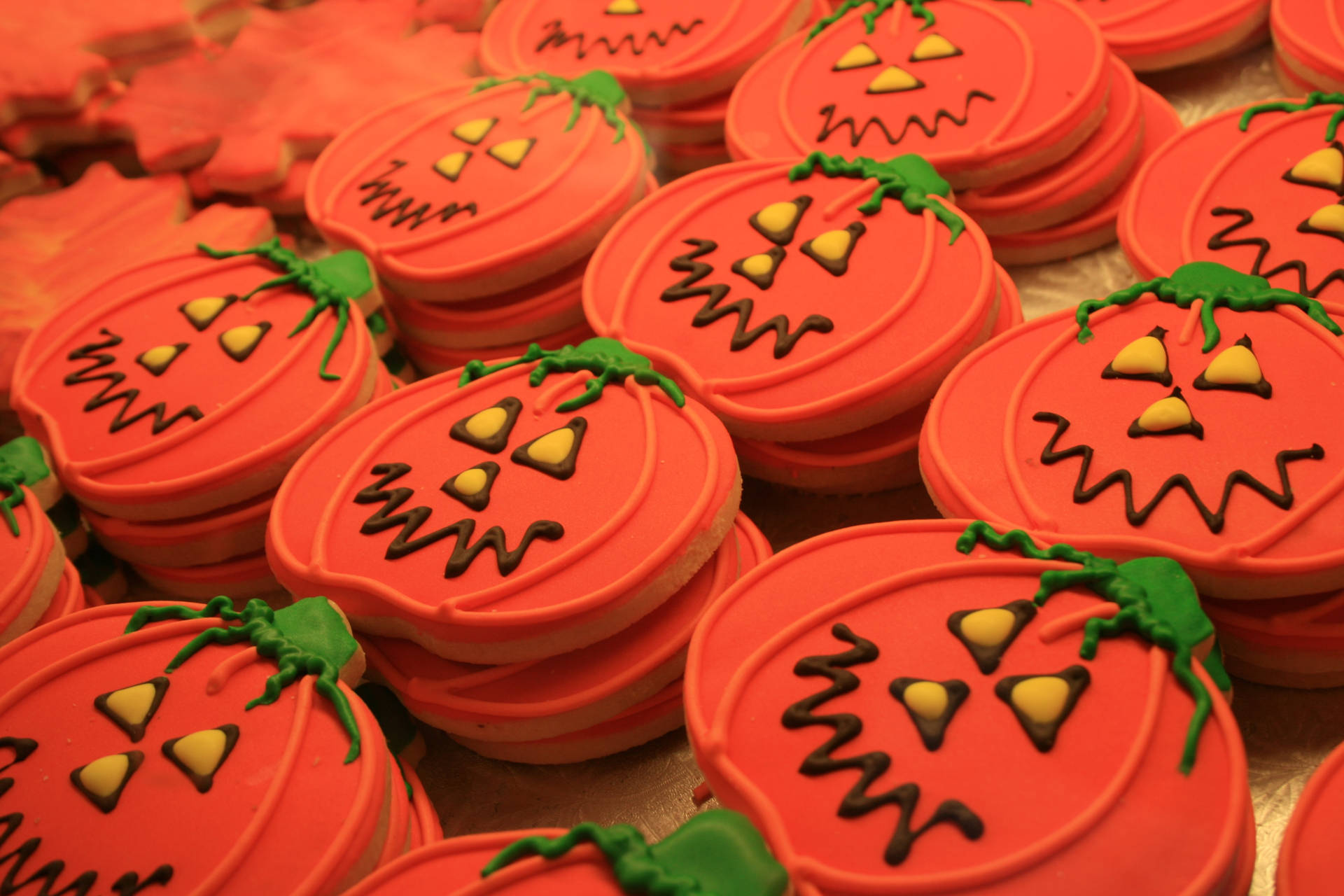CookiesFofos de Abóbora de Halloween Papéis de Parede — Pilhas de biscoitos laranja brilhantes em forma de abóbora com hastes verdes e rostos assustadores de chocolate.