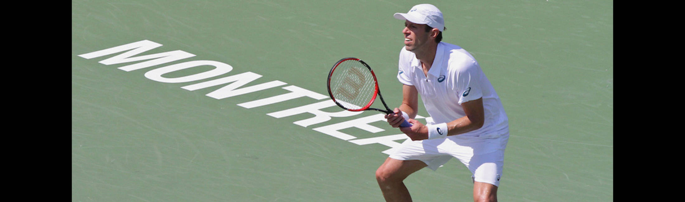 DanielNestor Agachado. Papéis de Parede — Um tenista masculino com equipamento branco se prepara para bater uma direita em uma quadra verde com 'MONTREAL' pintado em branco.