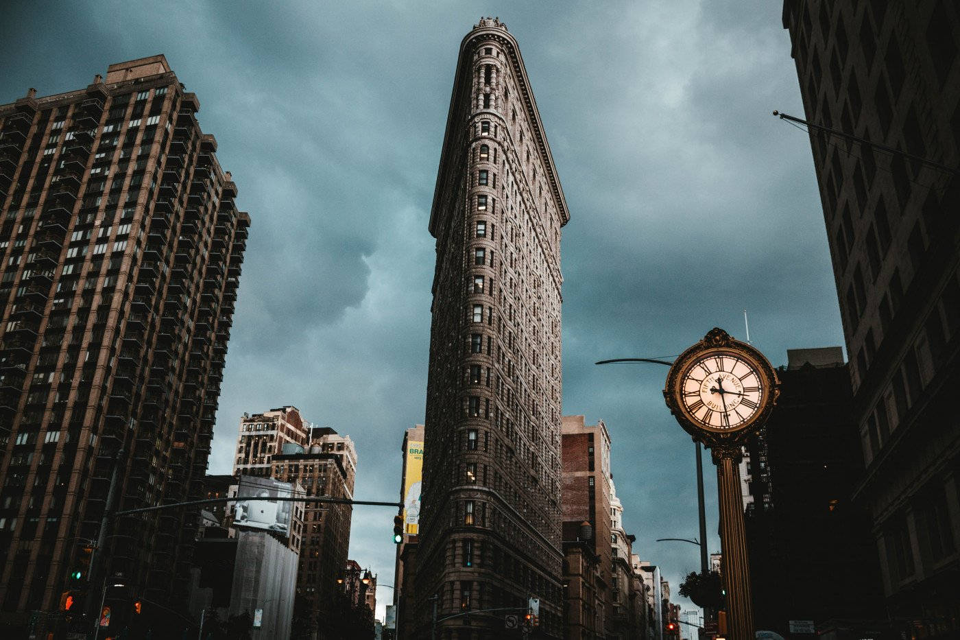 Dette er et bilde av Flatiron Building i New York under en skyet himmel, med en klokke synlig til høyre.
