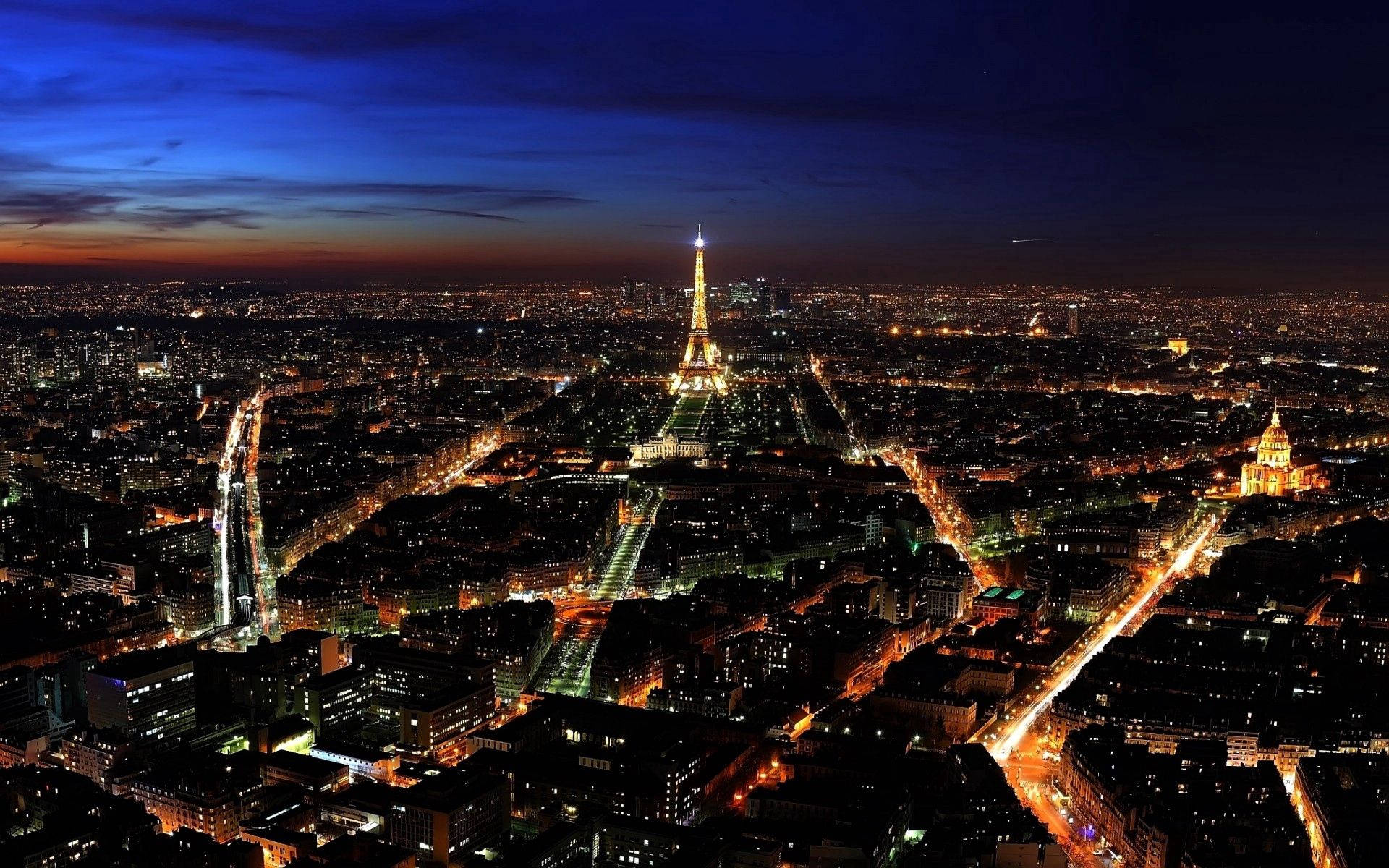 Paisaje urbano de París al atardecer con la Torre Eiffel iluminada y calles brillando con luces cálidas.