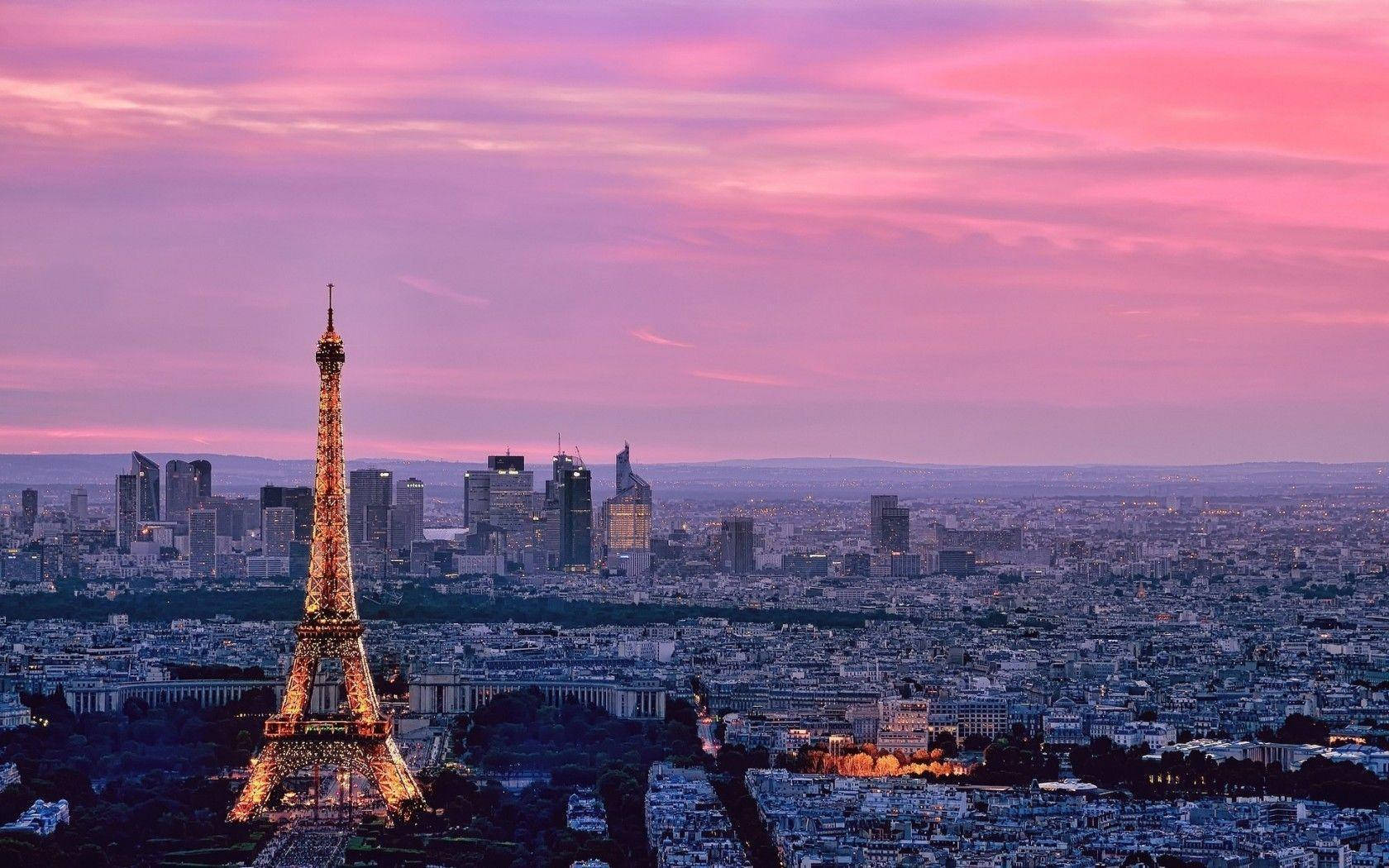 Torre Eiffel iluminada al anochecer con cielo rosa sobre el paisaje urbano de París.