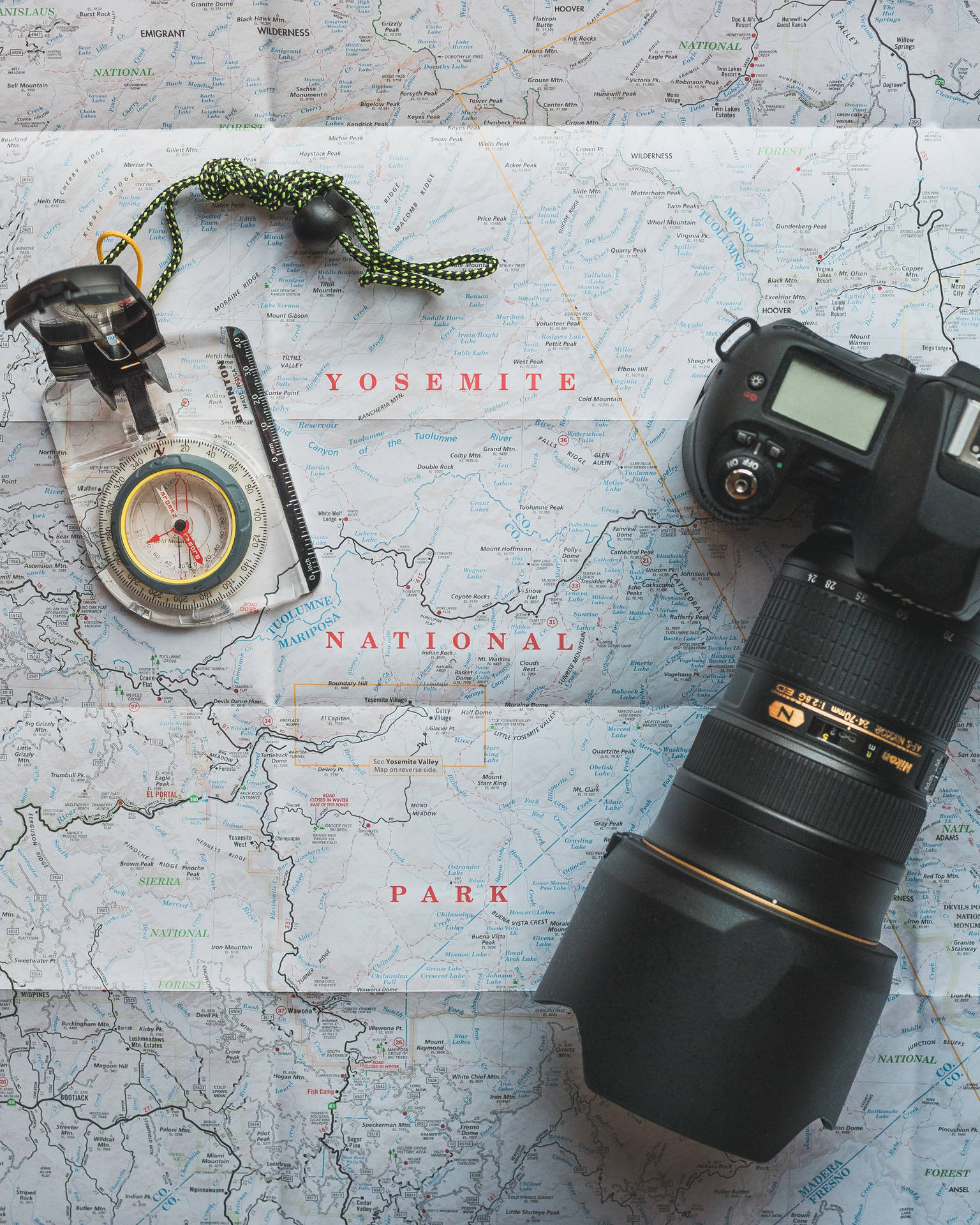 Encontresua bússola e sua aventura. Papéis de Parede — Uma câmera DSLR e uma bússola descansam sobre um mapa detalhado do Parque Nacional de Yosemite, prontos para aventura.