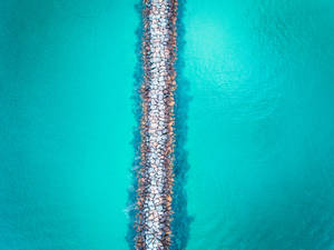 Vista aérea de un rompeolas de piedra en agua oceánica turquesa.