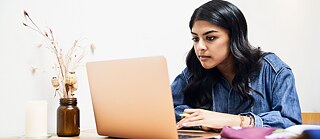 Eine junge Frau arbeitet konzentriert am Laptop.