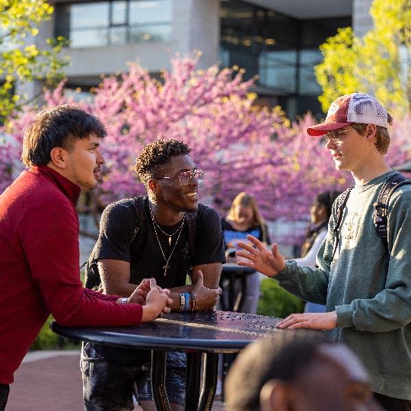 Three students having a conversation at a table outside The Hub.