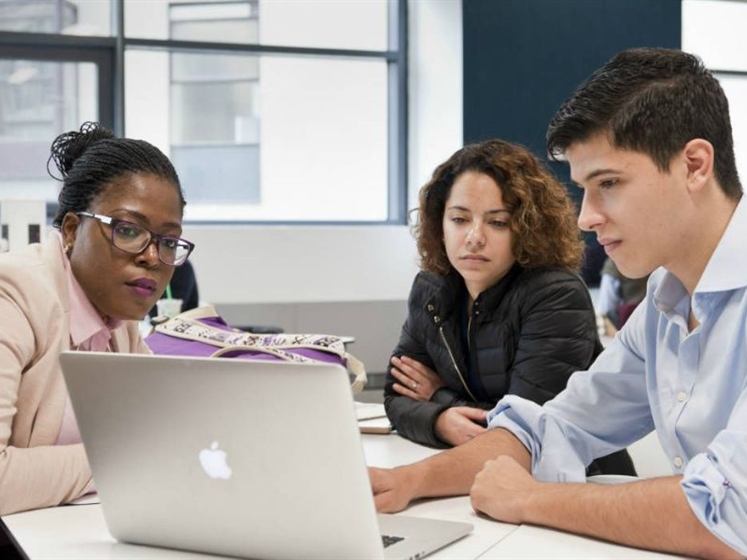 Three students sat together looking at a laptop