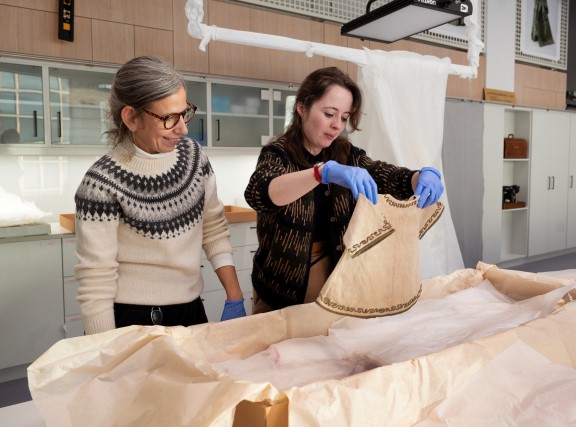 Two women unpacking baby clothes from boxes in a museum