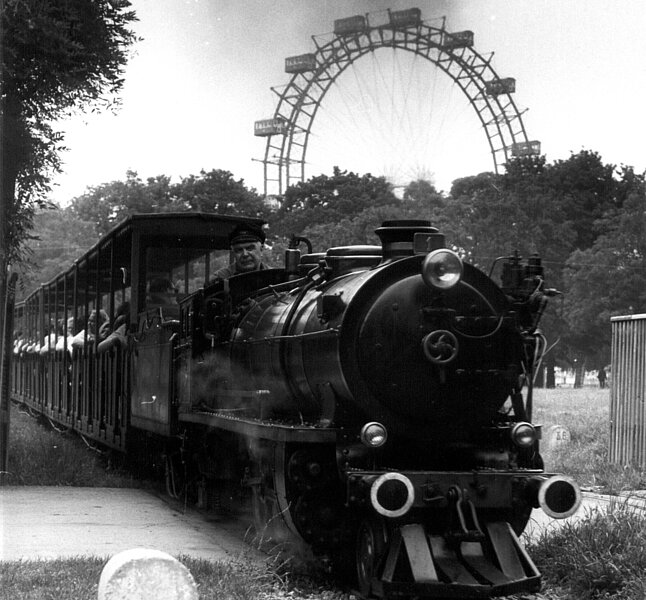 Schwarz-Weiß Foto einer Bahn, die auf Schienen fährt. 