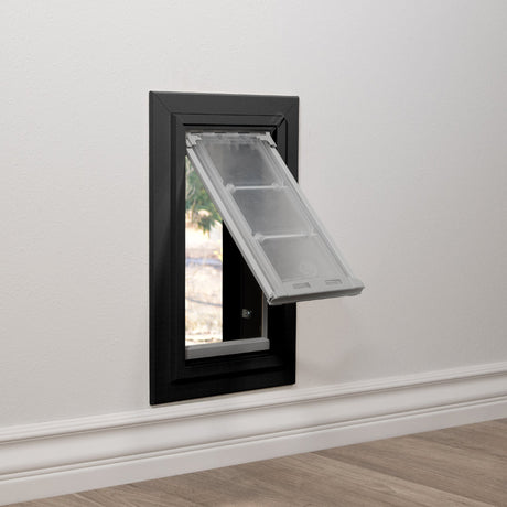 Endura Flap black double-flap pet door for thick walls, dual pane clear flap swung outward at 45 degrees, beveled trim surround with the through-wall tunnel and a locking knob visible inside.