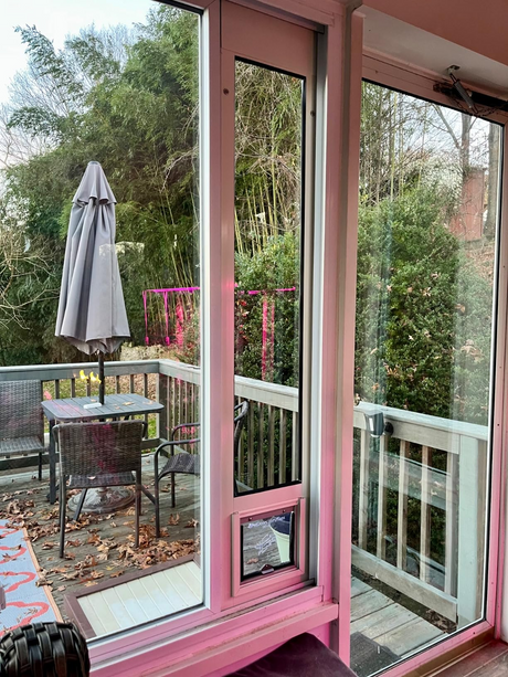 Liberty Cat Door for horizontal sliding windows, two white pet door inserts in a residential slider with a magenta aluminum frame, viewed from inside with the patio beyond.
