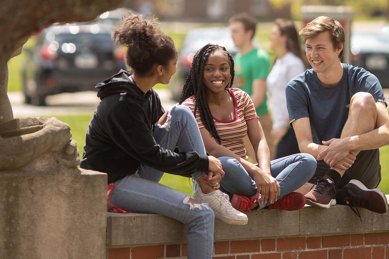 Three people sitting on a ledge.