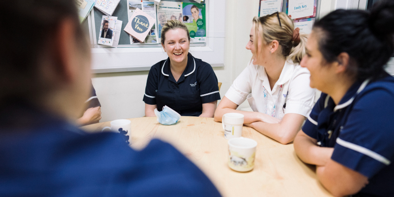 Image of nurses smiling and talking around a table
