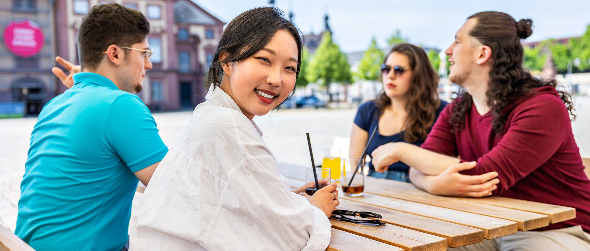 CHE-Ranking 2026 Vier Studierende sitzen an einem Café-Tisch. Eine Person schaut in die Kamera. Im Hintergrund ist ein Teil des Schlosses zu sehen.