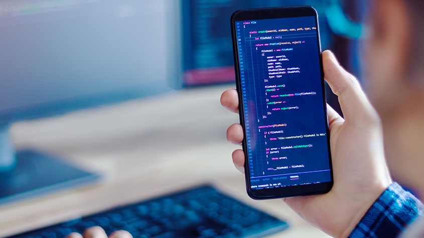personne tenant un téléphone portable avec un code de développement symbolisant l’utilisation de la propriété intellectuelle pour le développement d’applications mobiles
