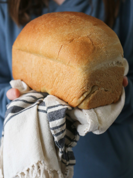 Someone holds a loaf of honey whole wheat bread with a linen tea towel