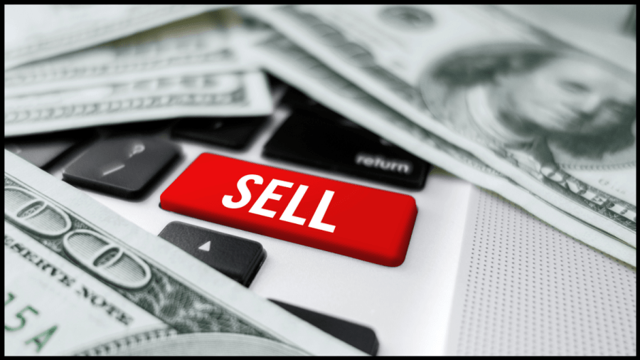 Photo of a computer keyboard with the shift key is red with the word Sell on it. Money is spread around.