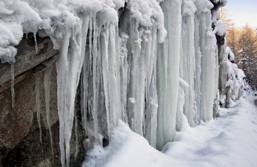 a bunch of thick icicles hanging from a snowy rock edge