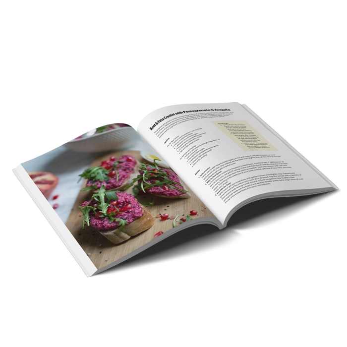 Un livre de cuisine à couverture souple au format portrait s'ouvrant sur une recette de tartelettes à l'orange et aux myrtilles et avec une photo en montrant trois.
