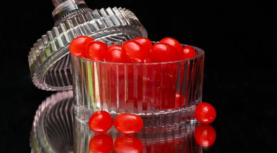 Bright red jelly beans in crystal container with lid on black background