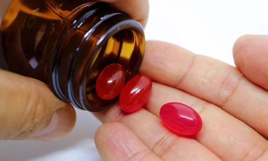 Hand pouring red capsules out of bottle into other hand