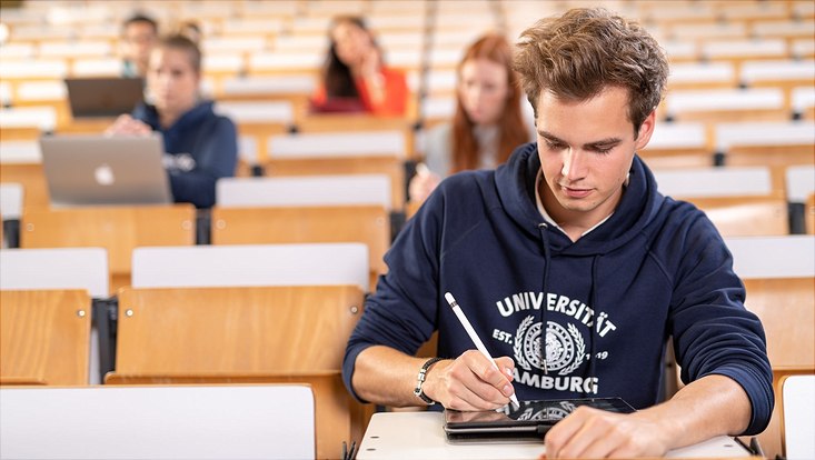 Ein Student sitzt im Hörsaal und schreibt.