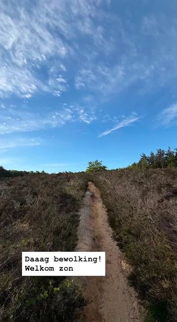 Welcome sun A narrow sandy path through heathland under a bright blue sky with scatterded clouds and sunlight breaking through