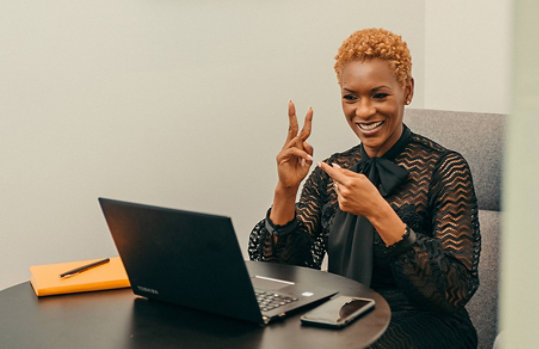 A woman using a laptop signs to an on-screen colleague. 