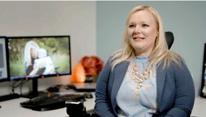 A woman who uses a wheelchair sits in front of her desk.