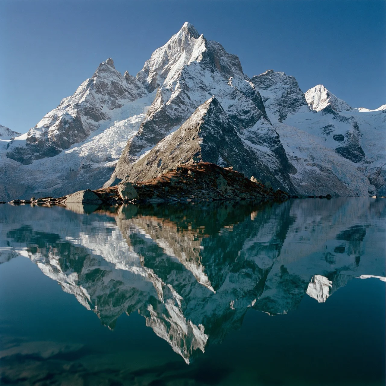 A crystal-clear mirror reflection of a towering mountain peak is perfectly captured on the glassy surface of an alpine lake.