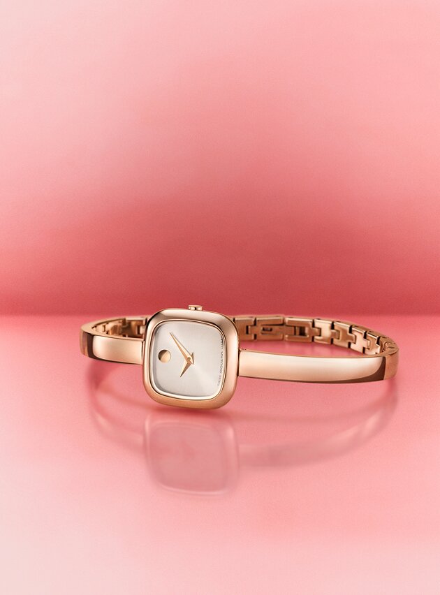 Square Museum Bangle watch laying on its side with a pink background.