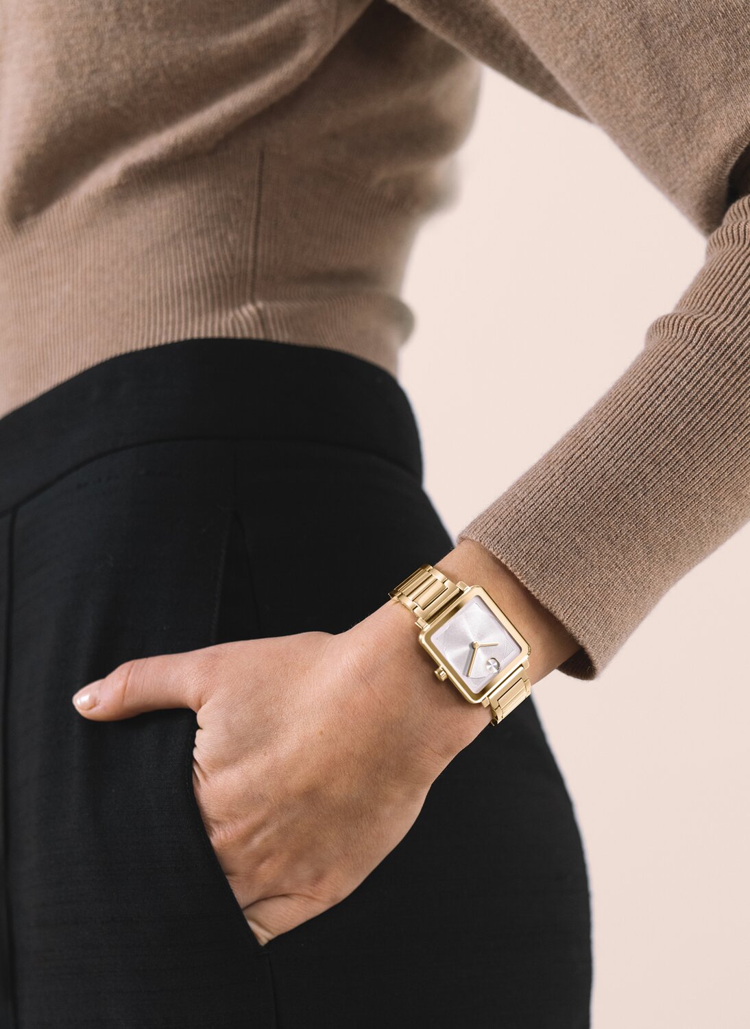 Woman in a brown sweater and black pants with her hand in her pocket wearing the gold tone BOLD Evolution 2.0 square watch