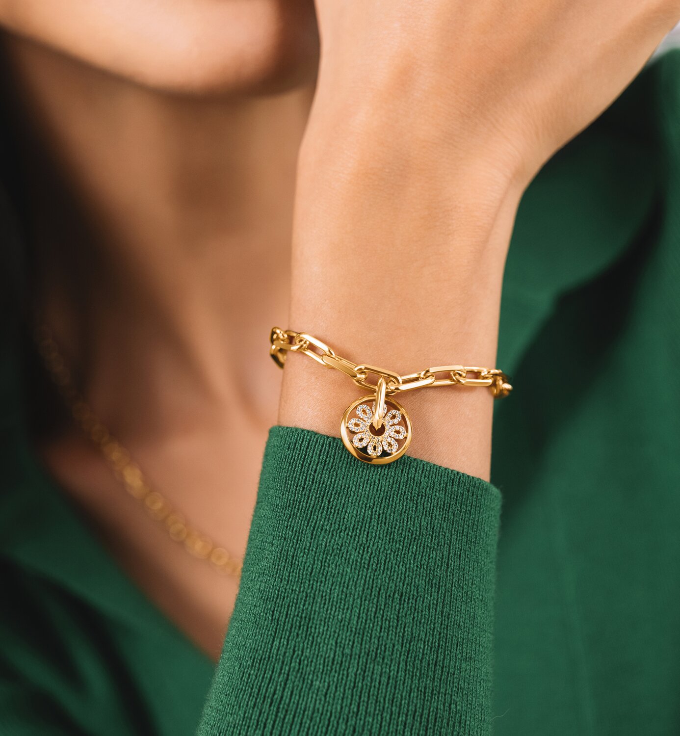 Woman in a green sweater wearing the gold tone Fleur bracelet featuring lab grown diamonds.