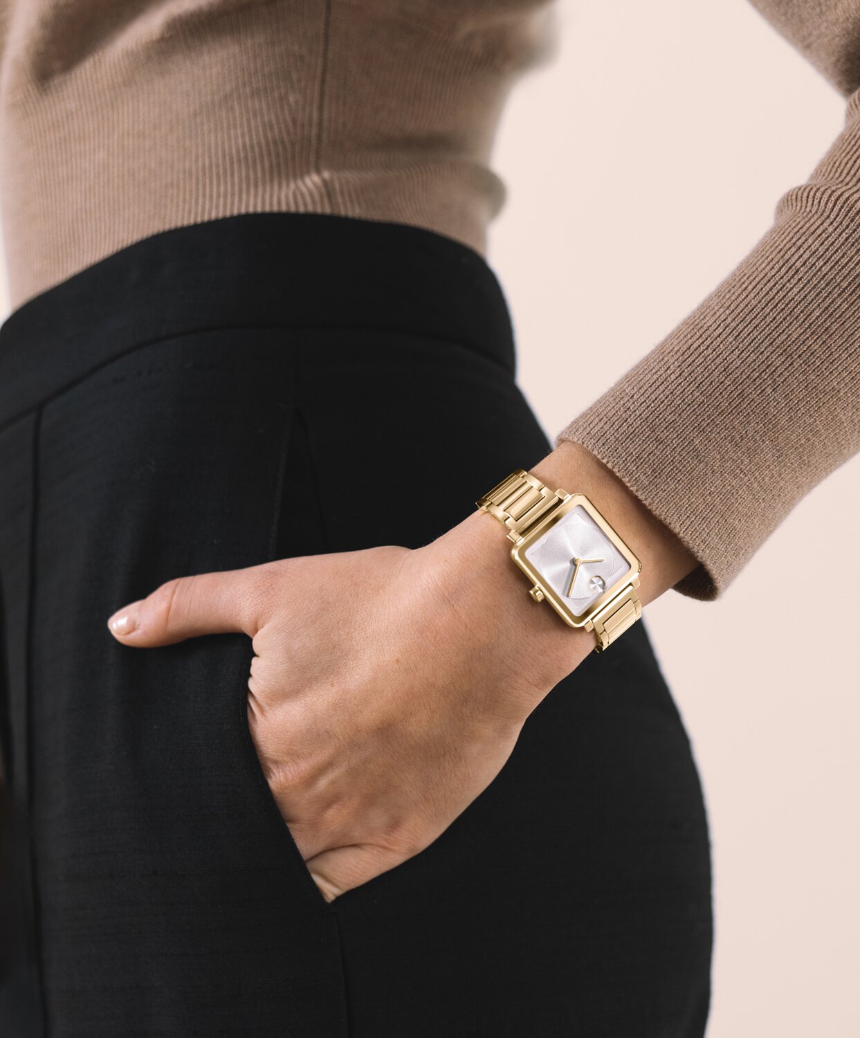 Woman in a brown sweater and black pants with her hand in her pocket wearing the gold tone BOLD Evolution 2.0 square watch