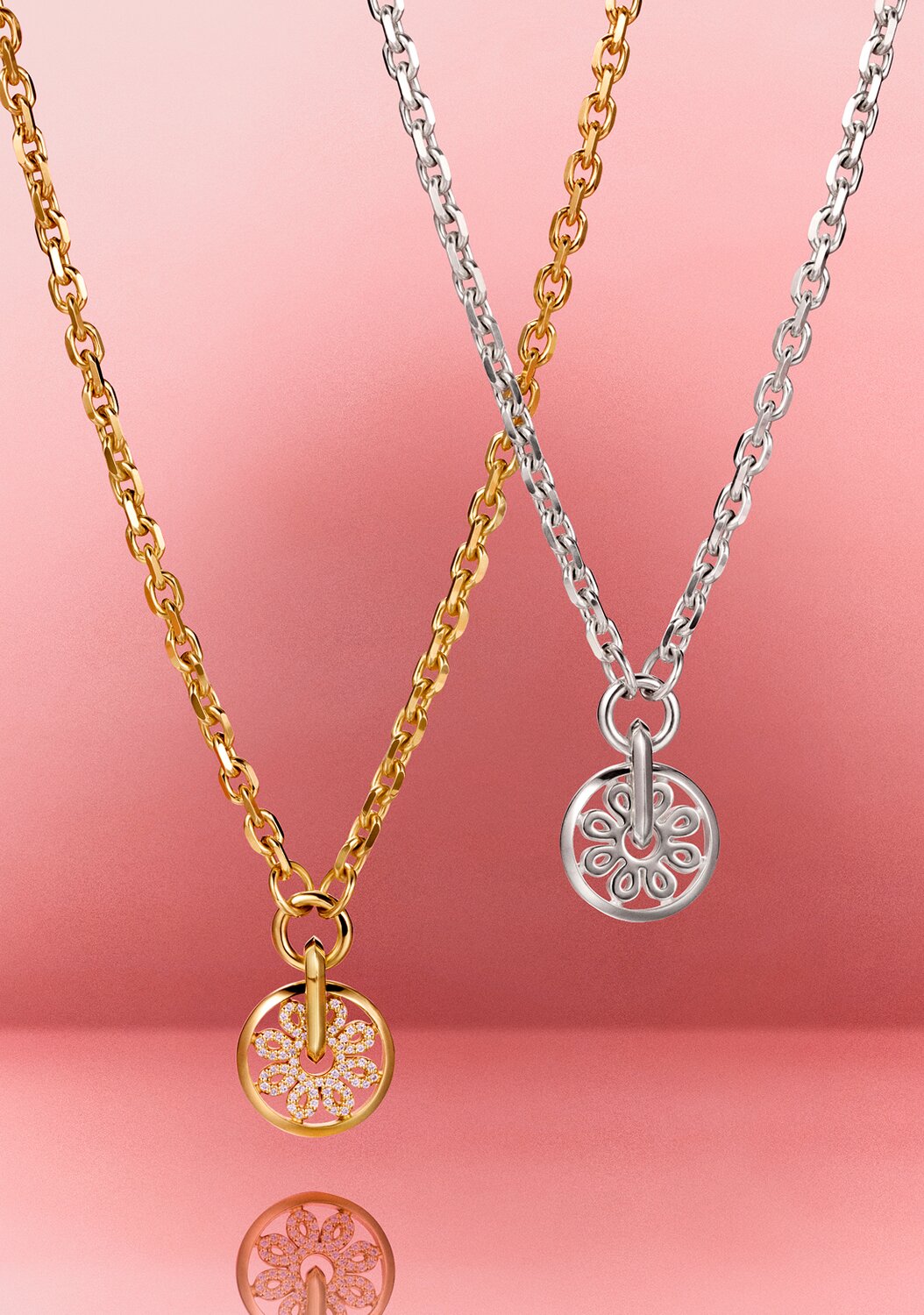 Gold tone Fleur necklace with lab grown diamonds hanging next to a silver Fleur necklace in front of a pink backdrop 