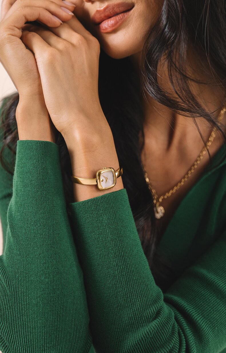Woman in a green sweater wearing the gold tone Museum Bangle Square watch.